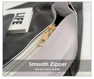 Detailed close-up of glossy white patent leather bag with gold metal zipper and stitching