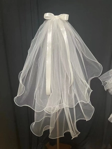 Detail of white double-layered bridal veil with pearl bow and curly edges on dark background