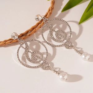 Sparkling music note drop earrings with rhinestones and pearl charms on beige background