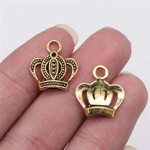 Detailed macro view of two gold crown-shaped metal jewelry pendants held by fingers