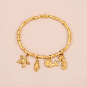 Dettaglio del bracciale a bambù dorato con ciondoli a stella marina conchiglia e balena