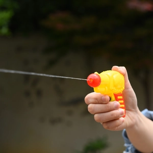 Close-up of yellow mini water gun for kids shooting water streams in a garden