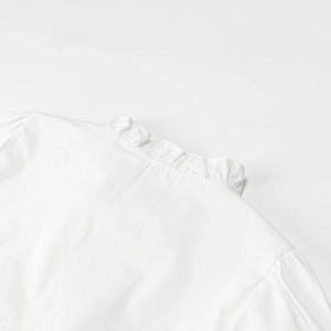 Close-up of white ruffled stand-up collar and delicate shoulder pleats on embroidery shirt