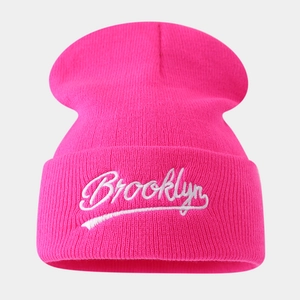 Close-up of white Brooklyn embroidery on a warm rose pink knitted beanie hat