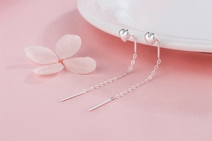 Detail of silver S925 heart tassel drop earrings on a soft pink background with ceramic decor