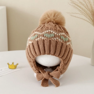 Detail of warm winter knit earflap hat with tan faux fur pom and jacquard pattern