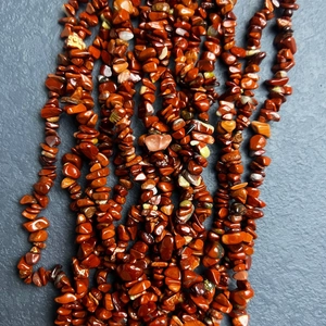 Close-up of irregular natural red jasper stone beads on a textured grey slate background