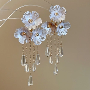 Detail von weißen Blumenohrringen mit langen Goldquasten und Kristallanhängern am Ständer