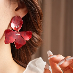 Detail of red resin flower earring with marble texture and rhinestones on model