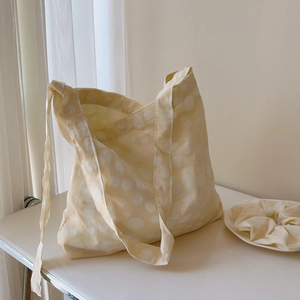 Detail of light yellow polka dot tote bag with matching scrunchie on a white surface