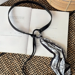 Detail of thin black leather belt with black and white paisley fabric tassel on book