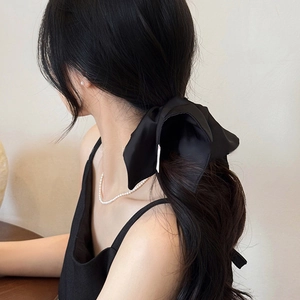 Detailed close-up of a large black satin bow hair tie worn on a low ponytail