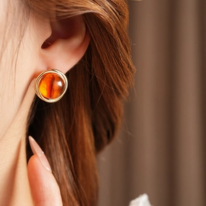 Close-up of a model wearing round amber resin earrings with elegant gold metal frames