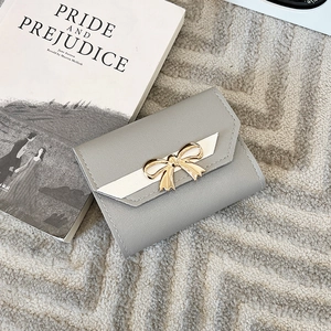Close-up of a grey leather tri-fold wallet with a golden bow on a textured carpet background