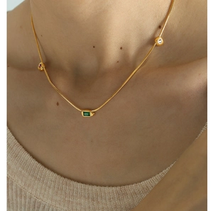 Macro detail of gold snake chain necklace featuring green, red, and white inset gemstones