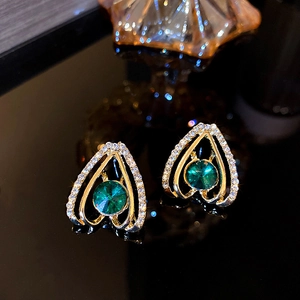 Macro shot of gold heart-shaped earrings with green gemstones and sparkling crystals