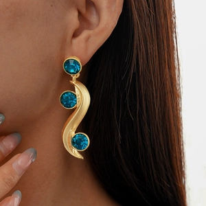 Detail of luxury gold wavy earrings featuring vibrant blue crystals worn by a model
