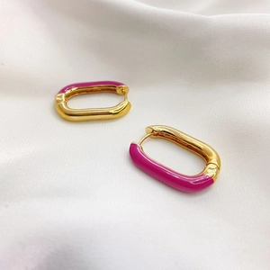 Detail of gold oval hoop earrings with pink enamel finish on white fabric