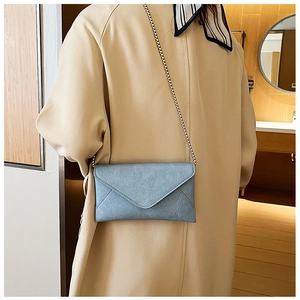 Detail of light blue-grey suede envelope crossbody bag with a delicate gold chain strap