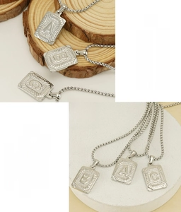 Macro shot of stainless steel square initial pendants A, B, C with radiant texture finish