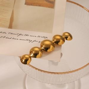 Minimalist gold beaded metal hair clip on a vintage glass tray with warm lighting