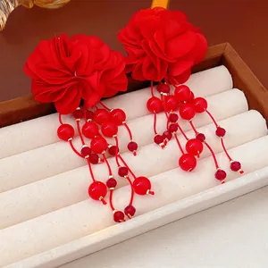 Élégantes boucles d'oreilles fleurs en tissu rouge avec pompons sur un présentoir
