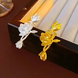 Elegant matte gold and silver lotus flower open rings shown on a wooden jewelry tray