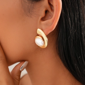 Close-up of gold geometric oval stud earring with white pearl inlay on model's ear