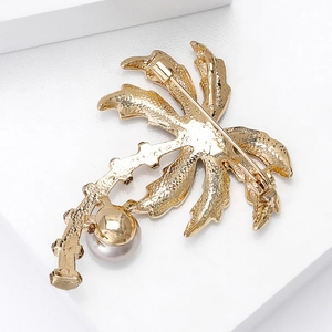 Golden coconut tree brooch with metallic leaf textures and pearl accent on white background