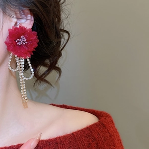 Close-up of red fabric flower earrings with sparkling rhinestone tassels worn by a model