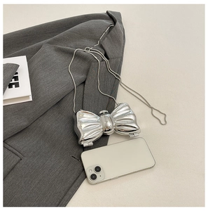 Detail of silver metallic bow-shaped mini evening bag with chain strap on beige surface