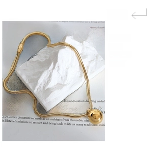 Macro view of gold plated round ball pendant on a sleek snake chain over white stone