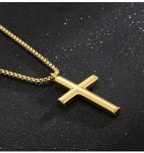 Close-up of a polished gold stainless steel cross pendant with a box chain on black texture
