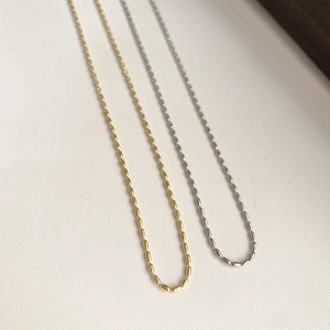 Detailed close-up of minimalist gold and silver rice-shaped links on a 18K titanium chain
