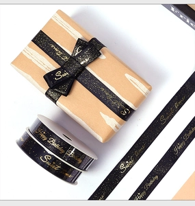 Detail of black satin ribbon with gold foil Happy Birthday text on gift box and roll