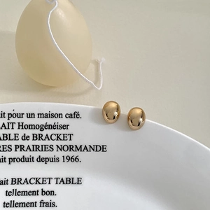 Polished gold oval stud earrings shown on a white ceramic plate with French text decor