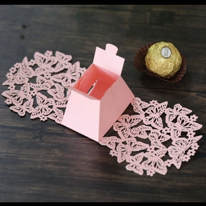 Detail of pink laser-cut butterfly wedding favor box with trapezoid structure on wood