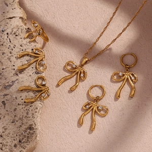 Close-up of gold bow jewelry set with zircon on natural stones and sand background