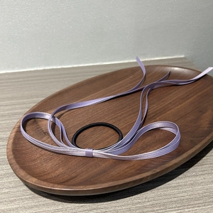 Detail of light purple satin ribbon bow on black elastic hair tie on wooden tray