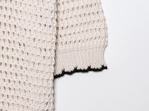 Detail view of cream crochet knit polo shirt featuring wave-patterned black cuffs