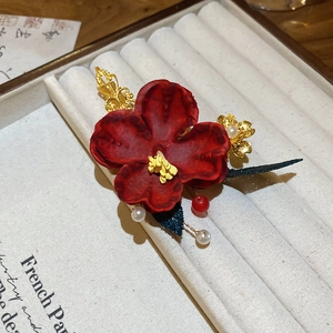 Close-up of red floral hairpin with golden leaf accents and hanging white pearls