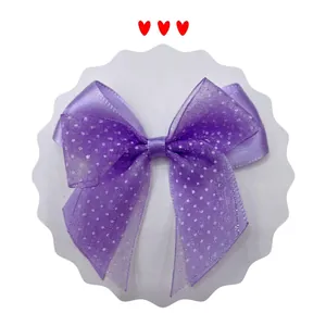 Close-up of a purple satin and polka dot mesh bow hair accessory on a white card