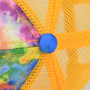 Dettaglio ravvicinato di un cappello trucker tie-dye con rete gialla e bottone blu superiore