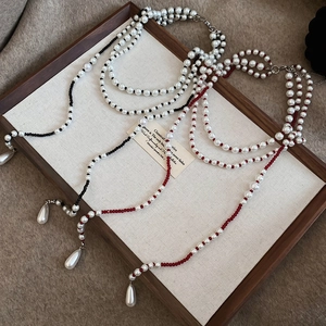 Detail of layered pearl necklace featuring small red beads and waterdrop pendants