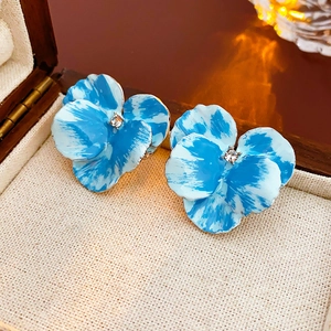 Dettaglio di orecchini a fiore blu e bianchi con cristalli in una scatola di legno