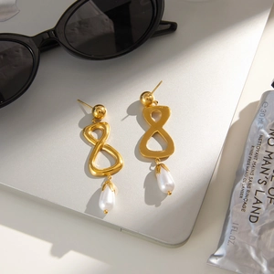 Détail de boucles d'oreilles signe infini doré avec perles poires sur surface métallique