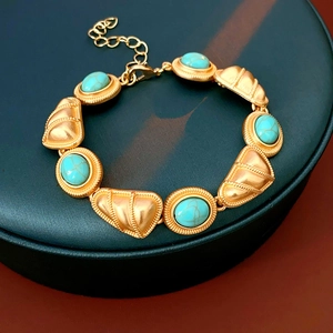Détail d'un bracelet vintage doré orné de pierres vertes sur un présentoir en cuir