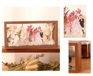 Detail of wooden shadow box frame with dried flowers and cartoon wedding couple figurines
