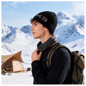 Dettaglio del berretto in maglia a coste con scritta SPRS jacquard su sfondo di montagne innevate
