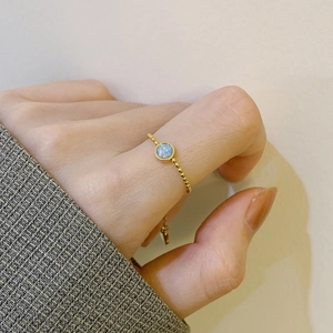 Adjustable gold bead ring with a blue opal stone shown on a finger with a gray suit